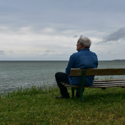 How Bereavement Service Can Help After Losing a Loved One, Man sitting on park bench in front of gloomy waterside view,