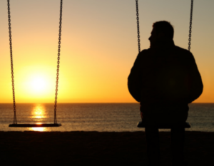 Man sitting on a swing looking at a sunset